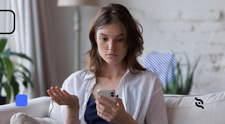 Mulher sentada em um sofá, com celular na mão e fazendo gesto de dúvida com as mãos.