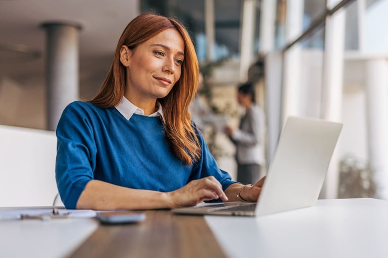 Mulher jovem e sorridente usando notebook em espaço de coworking com ambiente moderno e iluminação natural, representando inovação e tecnologia.