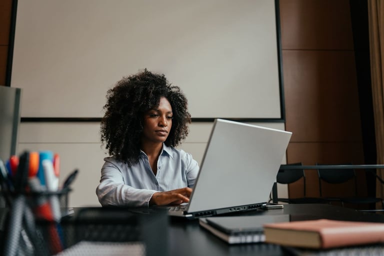 Secretária de escritório trabalhando com expressão focada em um notebook prateado.
