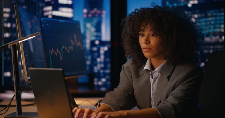 Executiva de negócios analisando gráficos de mercado enquanto trabalha em um escritório à noite com vista para cidade iluminada.