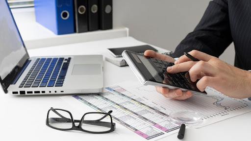 Pessoa calculando cobrança indevida com um computador e calculadora. 