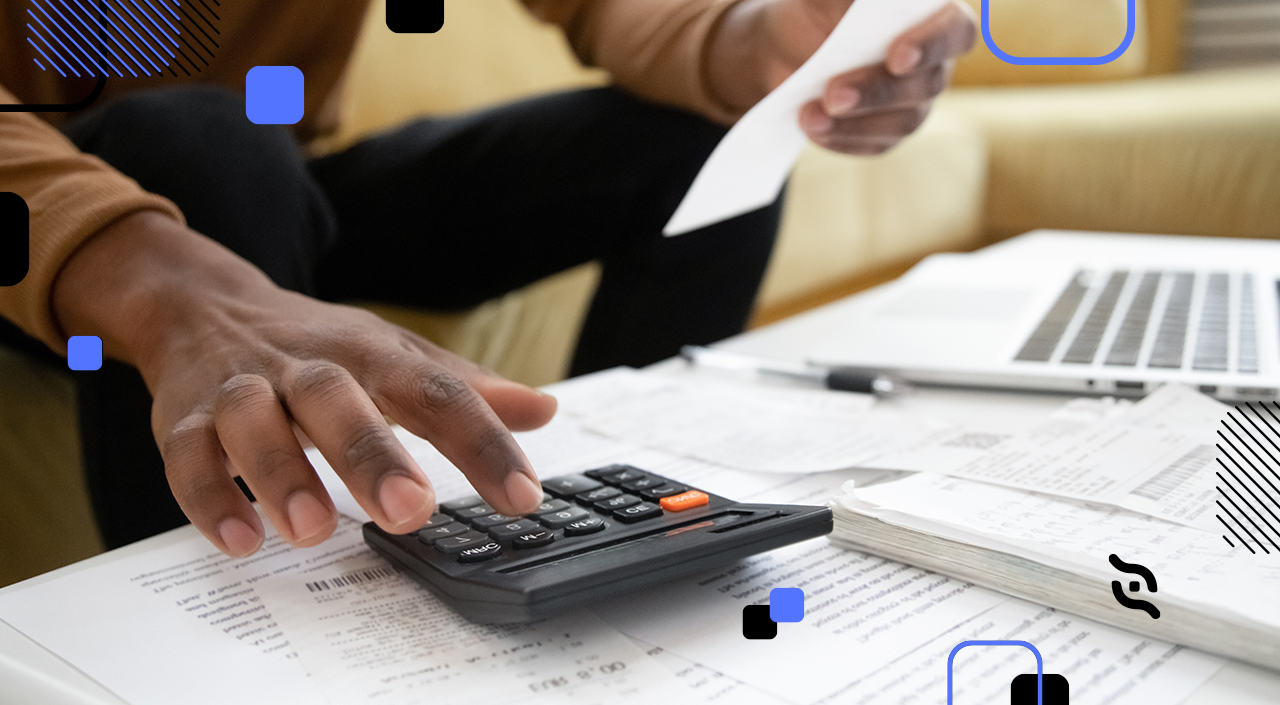 Mão mexendo em uma calculadora em mesa cheia de papéis.  