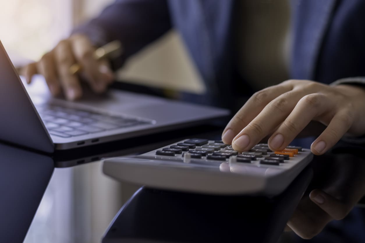 Pessoa usando calculadora e laptop durante trabalho de finanças ou contabilidade.