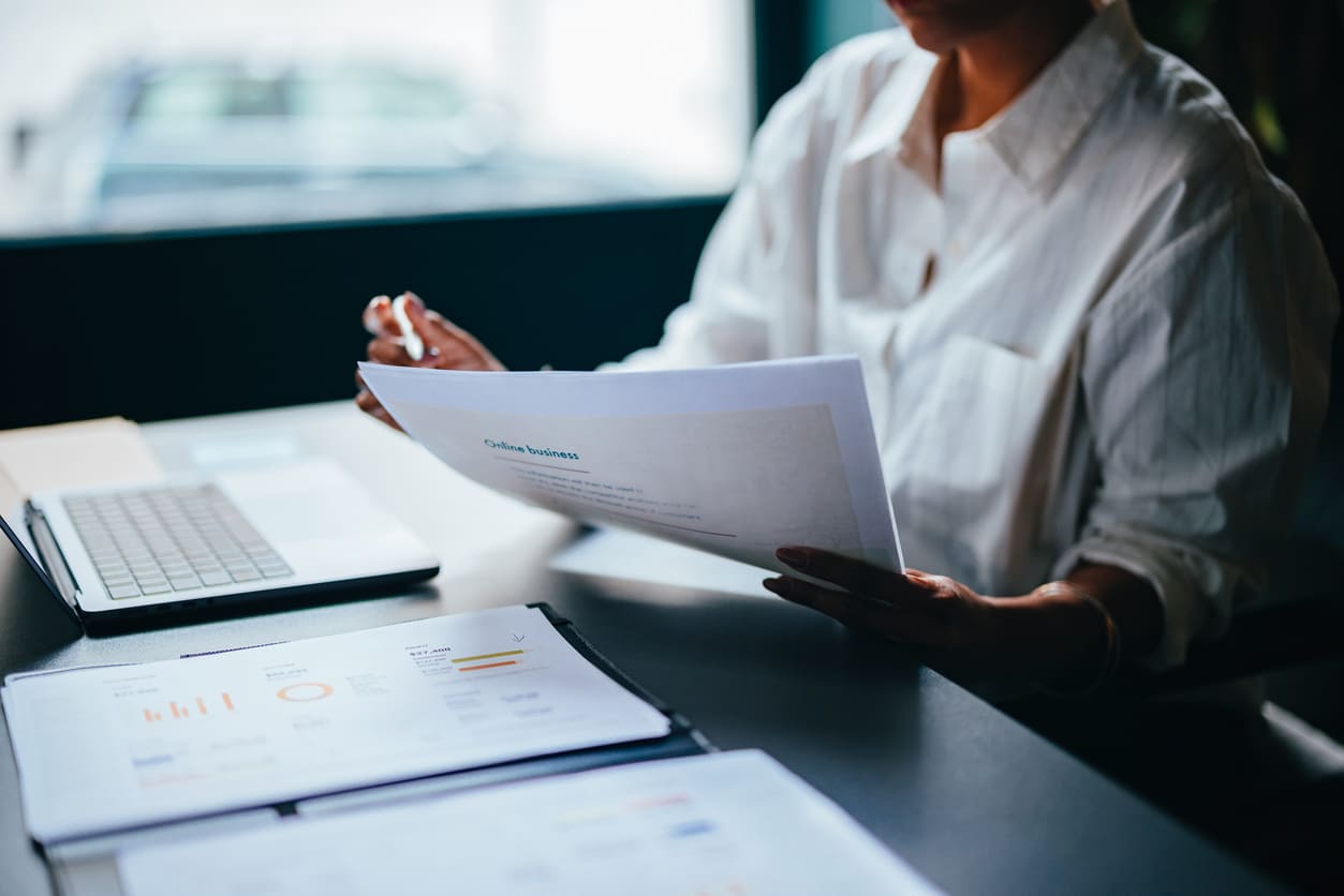 Pessoa analisando relatórios financeiros em ambiente de trabalho com computador e documentos, foco em negócios e planejamento estratégico.