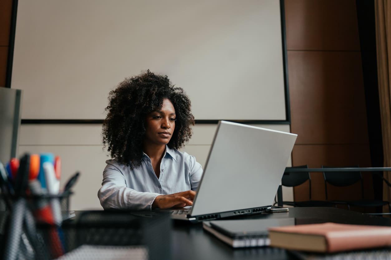 Secretária de escritório trabalhando com expressão focada em um notebook prateado.